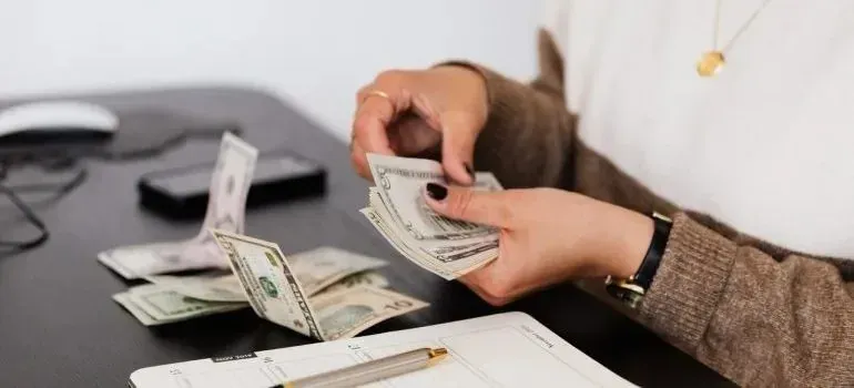 Person counting dollar bills at desk with open planner