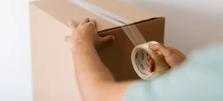 Person sealing cardboard box with clear packing tape