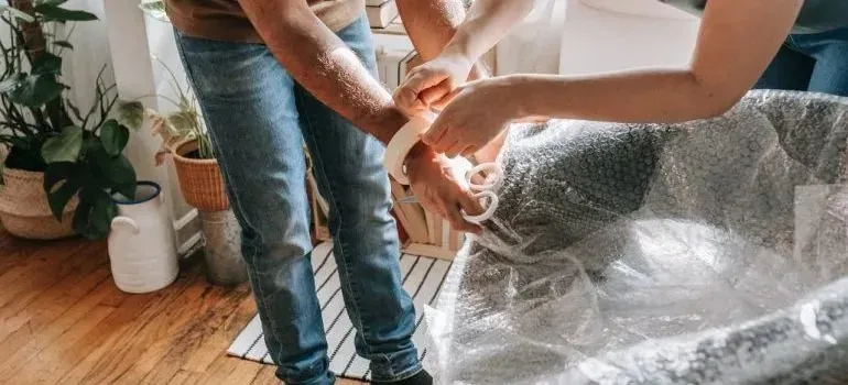 Couple wrapping household item in bubble wrap indoors