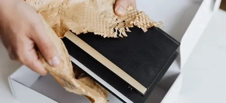Hands packing black notebooks with shredded paper filler into box