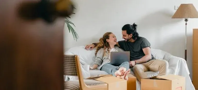 Smiling couple with laptop on sofa among moving boxes