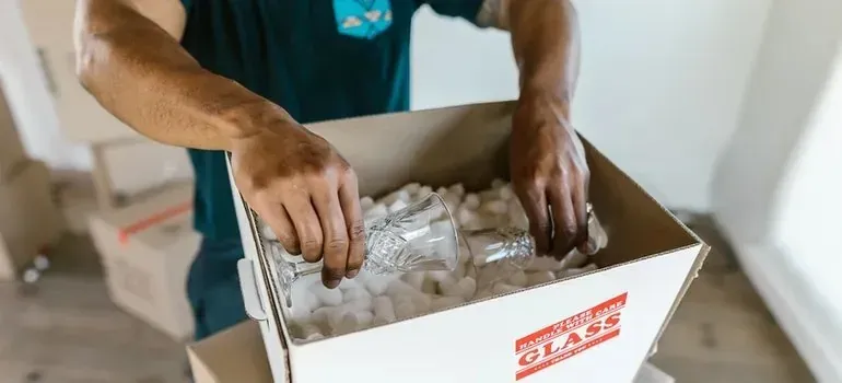 Mover packing crystal glass into box with foam peanuts