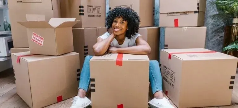 Smiling woman sitting among stacked moving boxes with fragile labels