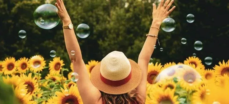Woman in straw hat celebrating in sunflower field with bubbles
