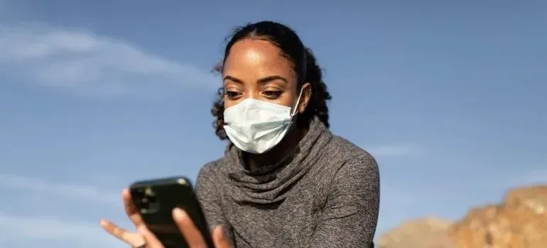 Masked woman checking smartphone outdoors under blue sky