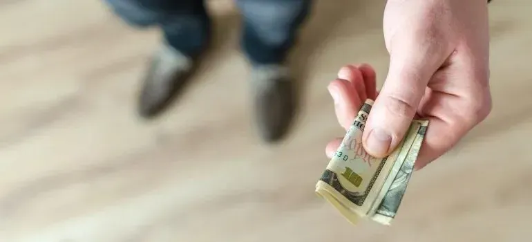 Hand holding folded dollar bills over wooden floor