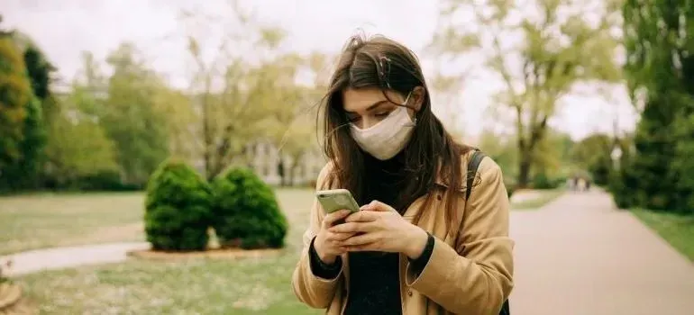 Masked woman texting on phone in green park