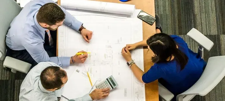 Three people reviewing blueprints at table