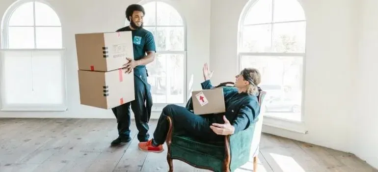 Mover bringing boxes to man relaxing in armchair