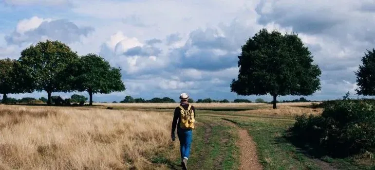 Person with backpack walking dirt path through golden field