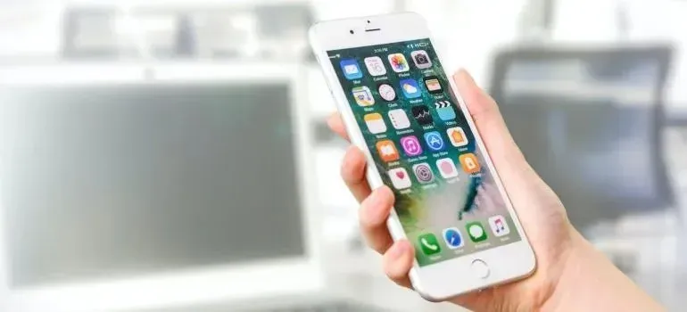 Hand holding smartphone showing app icons, blurred office background