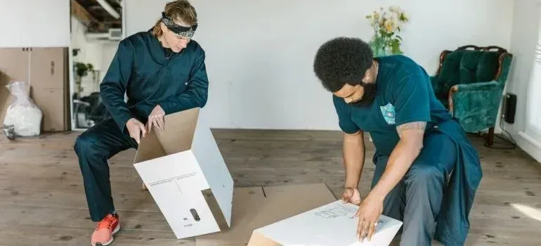 Two movers assembling flattened cardboard boxes in empty room