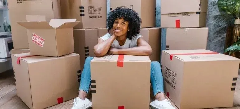 Smiling woman sitting among stacked moving boxes with fragile stickers