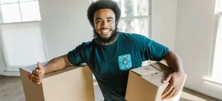 Smiling mover giving thumbs up while holding two boxes