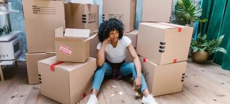 Tired woman sitting on floor surrounded by moving boxes