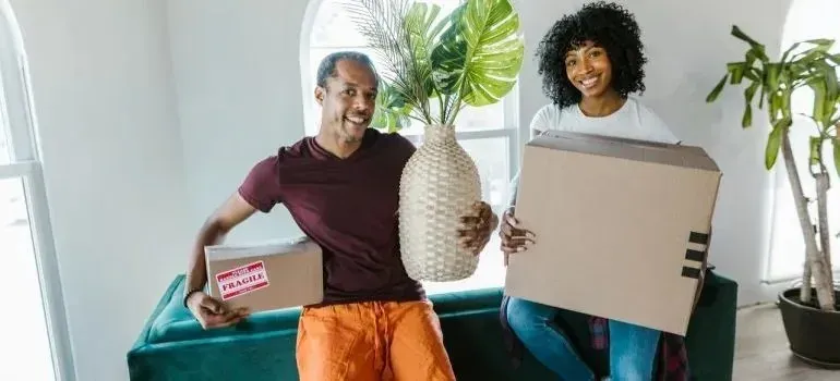Couple holding moving box and wicker vase with plant