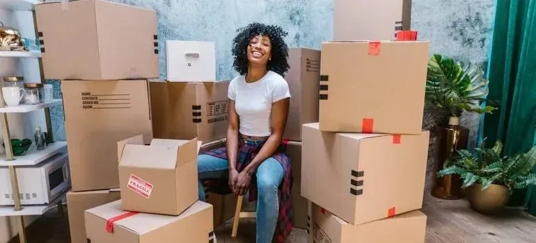 Smiling woman sitting surrounded by stacked cardboard moving boxes