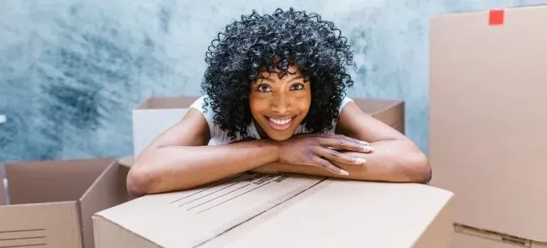 Woman resting head on arms atop cardboard moving box