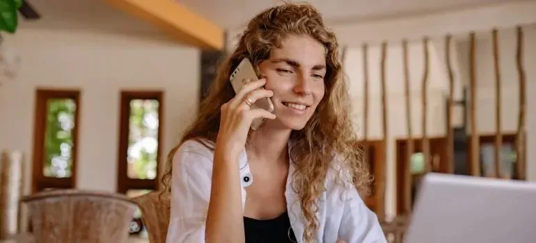 Smiling woman talking on phone while using laptop indoors