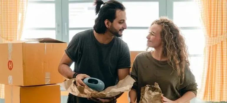 Couple unwrapping packed items beside cardboard moving boxes