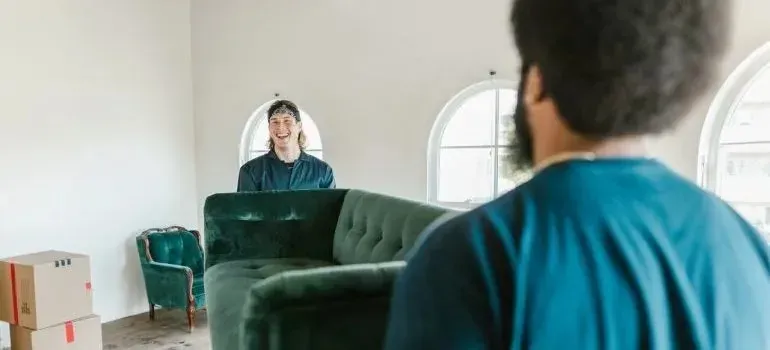 Two men carrying green sofa into bright living room