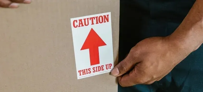 Hand applying caution this-side-up sticker to cardboard box