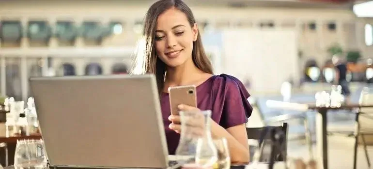 Smiling woman using phone and laptop at outdoor cafe