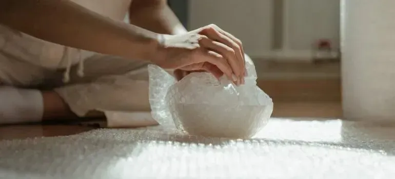 Hands wrapping an item in bubble wrap on floor