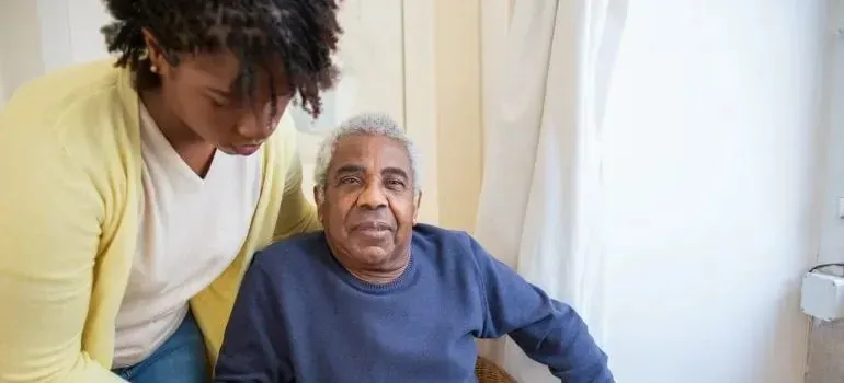 Young woman caring for seated elderly man at home