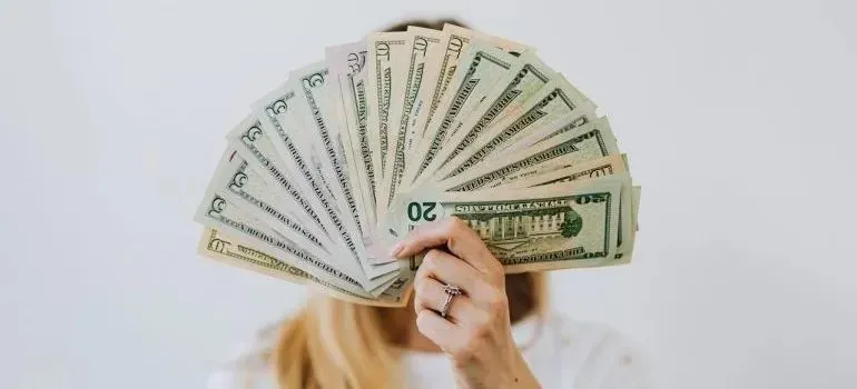 Woman holding fanned-out dollar bills covering her face
