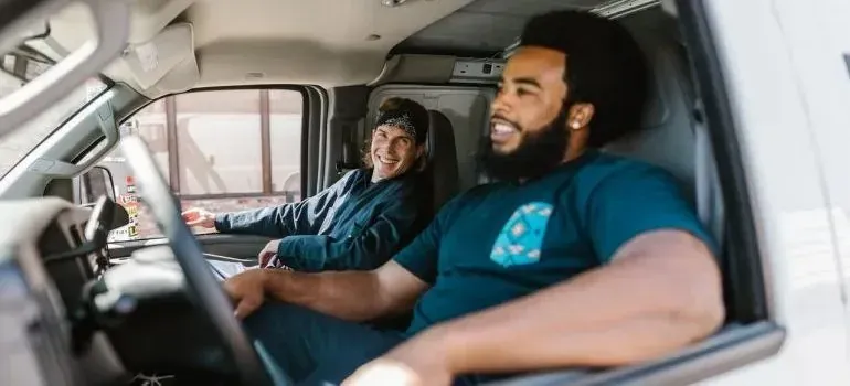 Two cheerful movers in van cab, unbranded shirts