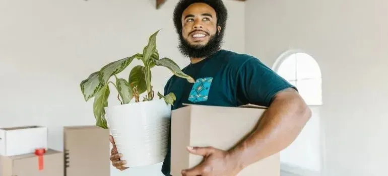 Smiling man carrying potted plant and cardboard box