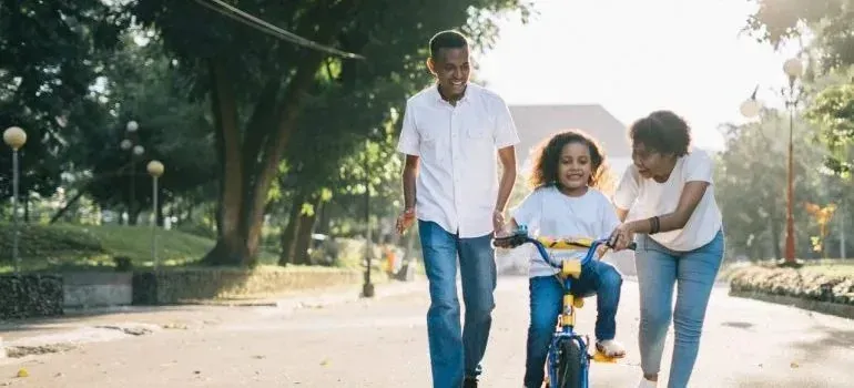 Parents helping child ride bike outdoors