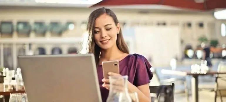 Woman using phone and laptop at outdoor cafe