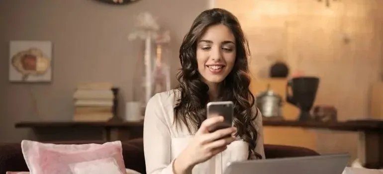 Young woman smiling at smartphone in cozy living room