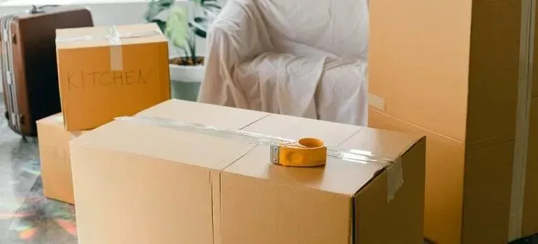Taped moving boxes, one labeled kitchen, beside covered chair