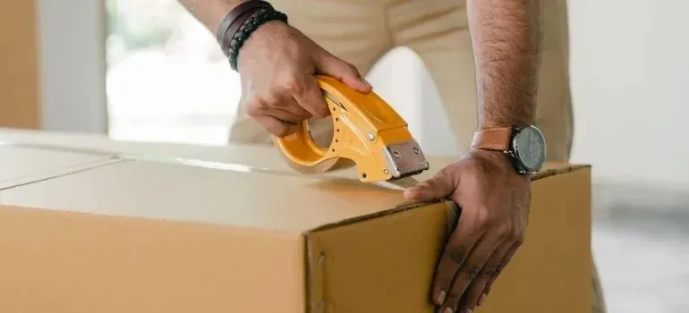 Hands sealing cardboard box with yellow tape gun
