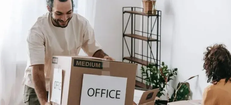 Man carrying medium moving box labeled OFFICE