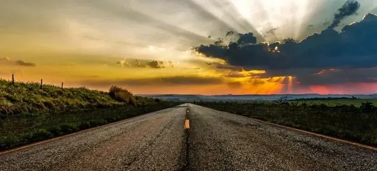 Empty rural road stretching toward dramatic sunset sky