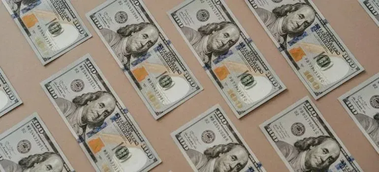 Hundred-dollar bills arranged in rows on beige background