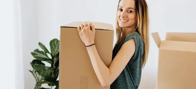 Smiling woman carrying large cardboard moving box