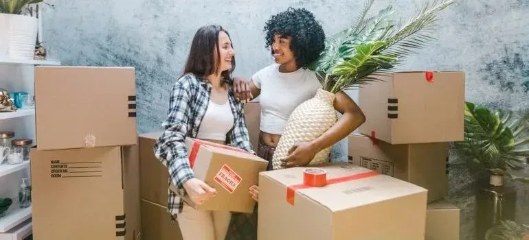 Two women unpacking boxes and houseplant vase indoors