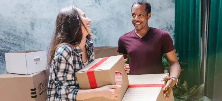 Cheerful couple carrying taped boxes with fragile labels