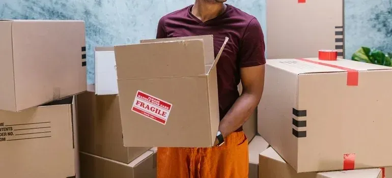 Man holding box with generic fragile sticker among boxes