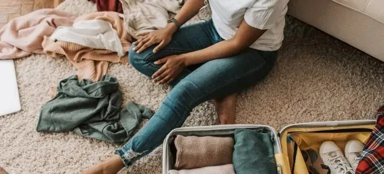 Woman on carpet packing clothes into open suitcase