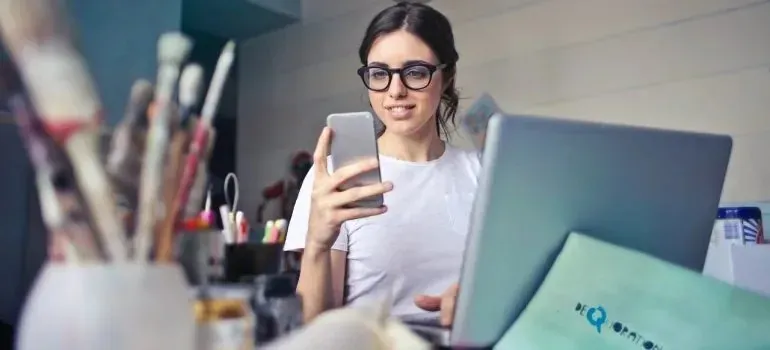Woman with glasses using smartphone at craft workspace