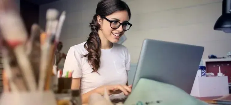 Smiling woman with glasses typing on laptop