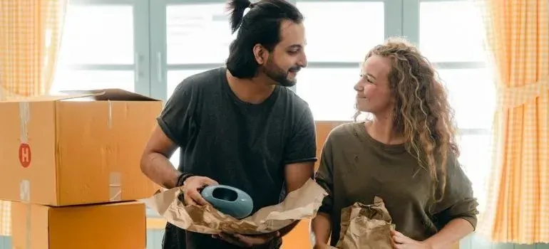Couple unwrapping packed items beside moving boxes