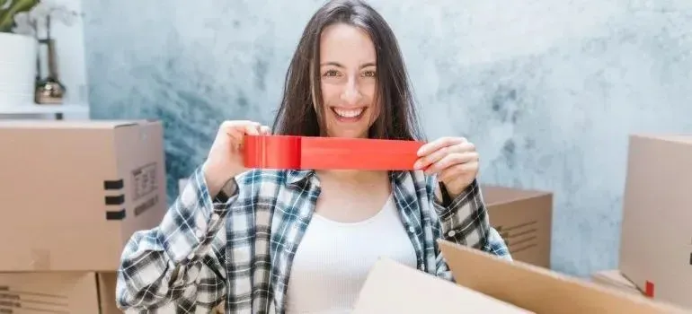Smiling woman holding red packing tape among boxes