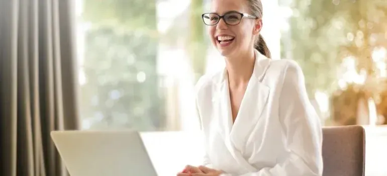 Laughing businesswoman in white blazer working at laptop